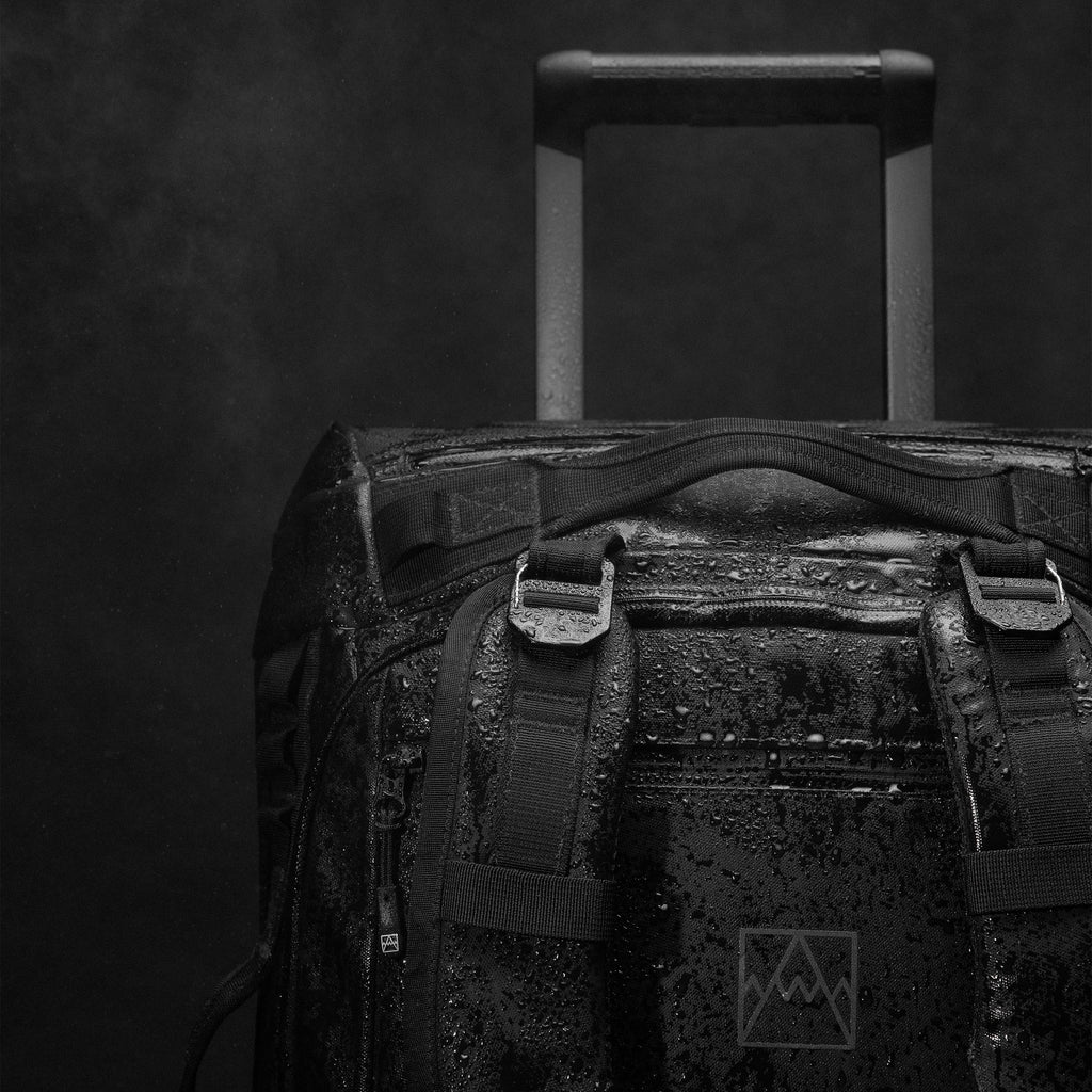 A close up studio shot of the g-hooks and detachable shoulder straps and telescopic handle on the Wheeled Kit Bag 40L in All Black