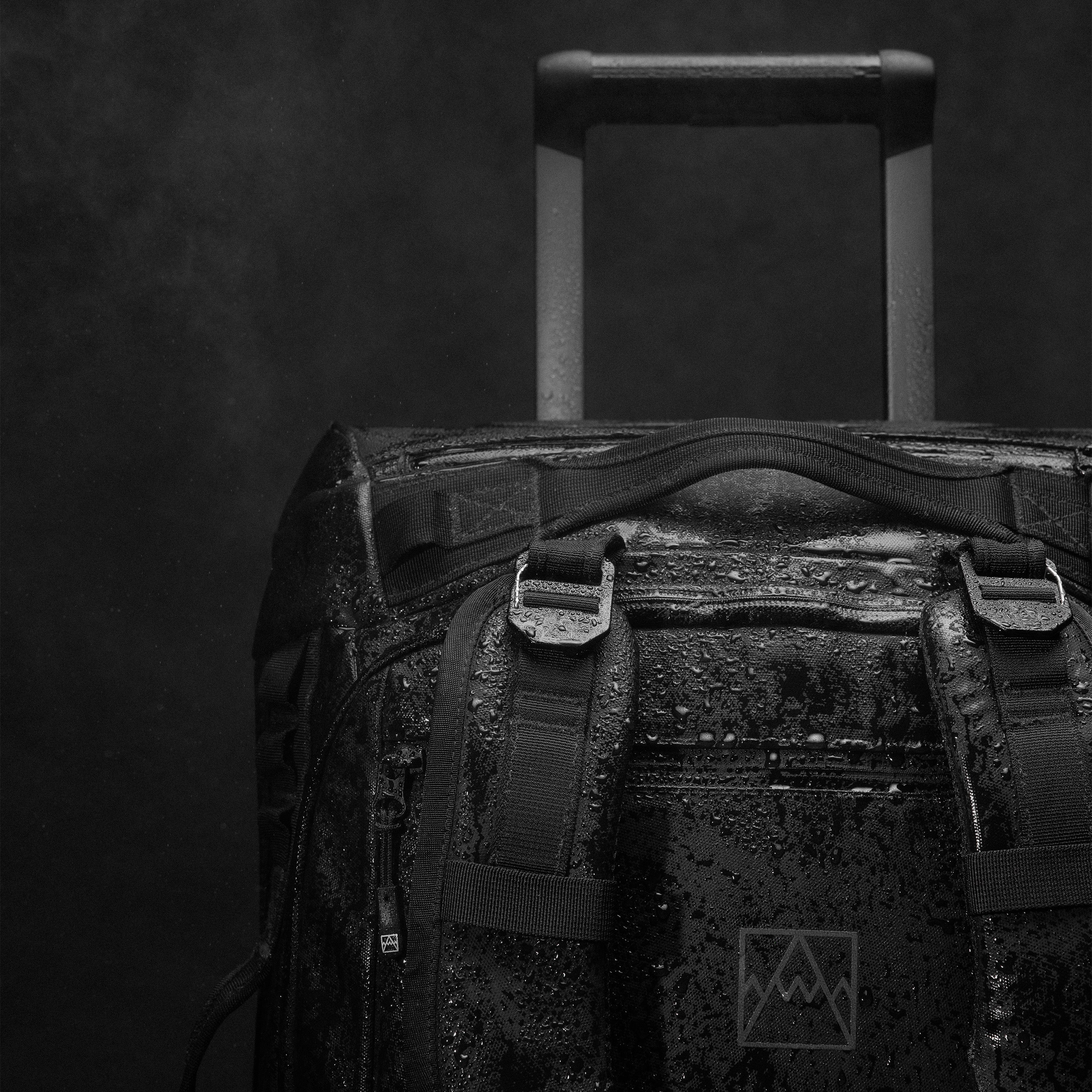 A close up studio shot of the g-hooks and detachable shoulder straps and telescopic handle on the Wheeled Kit Bag 40L in All Black